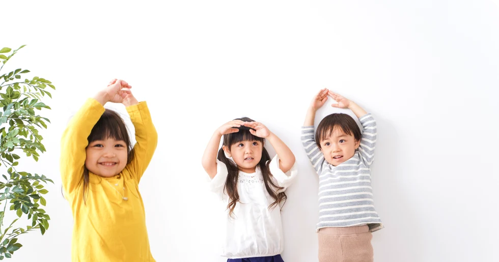 両手を挙げてポーズをとる3人の子どもたち